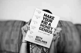 girl holding a copy of the book Make Your Kid a Money Genius over her face